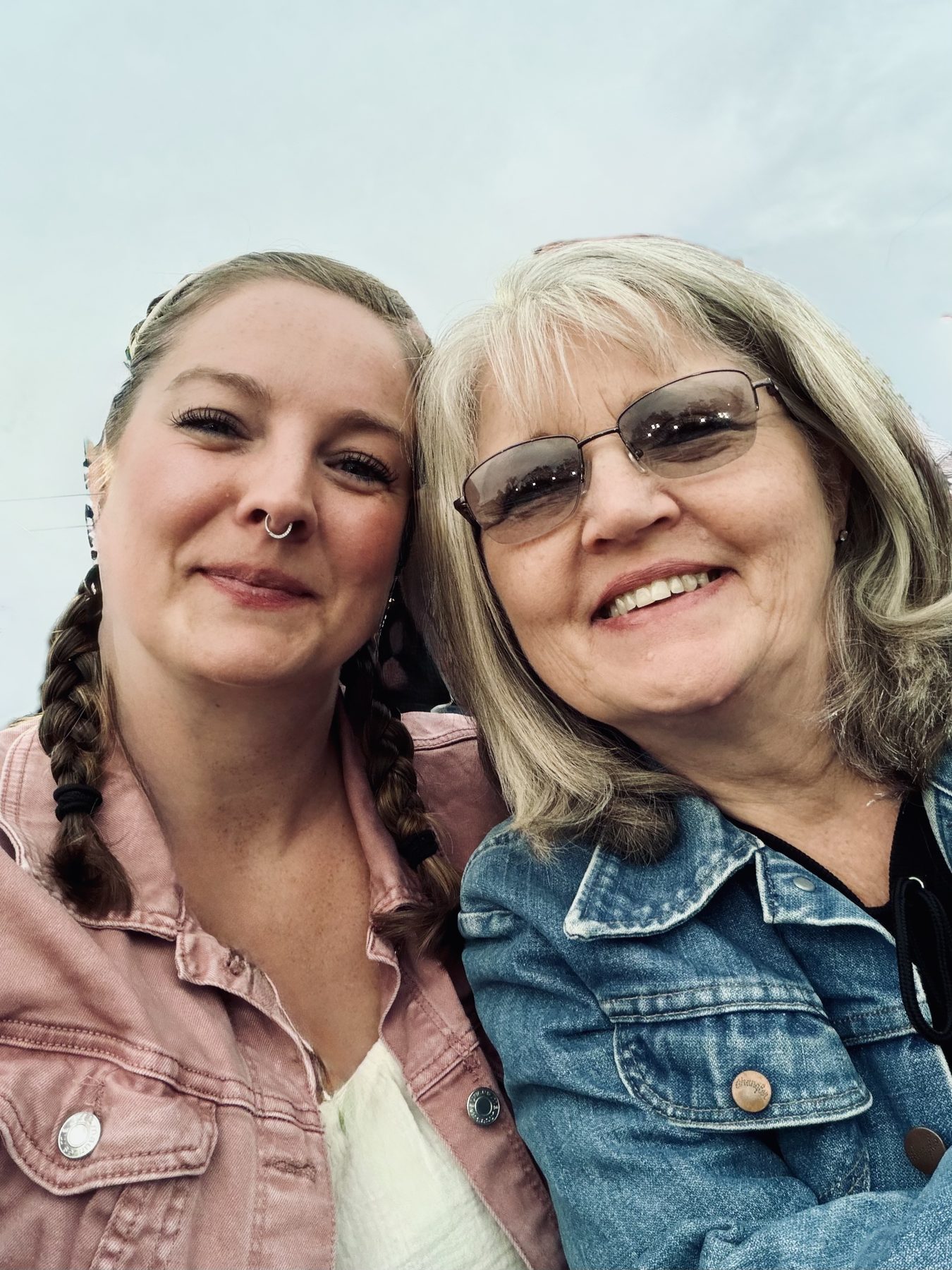 Aleasha in a pink denim jacket leaning cheek to cheek with her mother, who wears a denim jacket and sunglasses.
