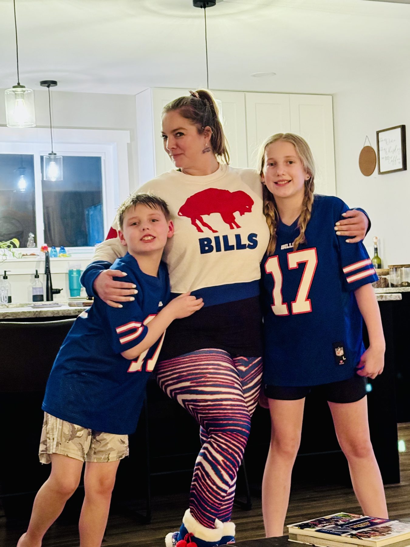 Aleasha in a Bills sweatshirt and striped leggings posing with two children in Bills jerseys.