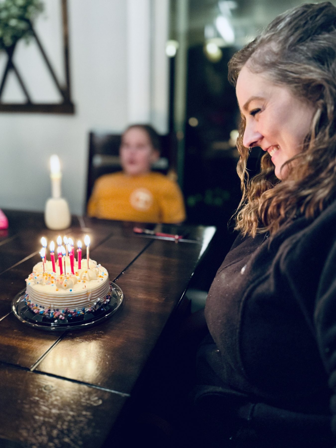 Aleasha smiling in profile at a birthday cake lit with pink candles.