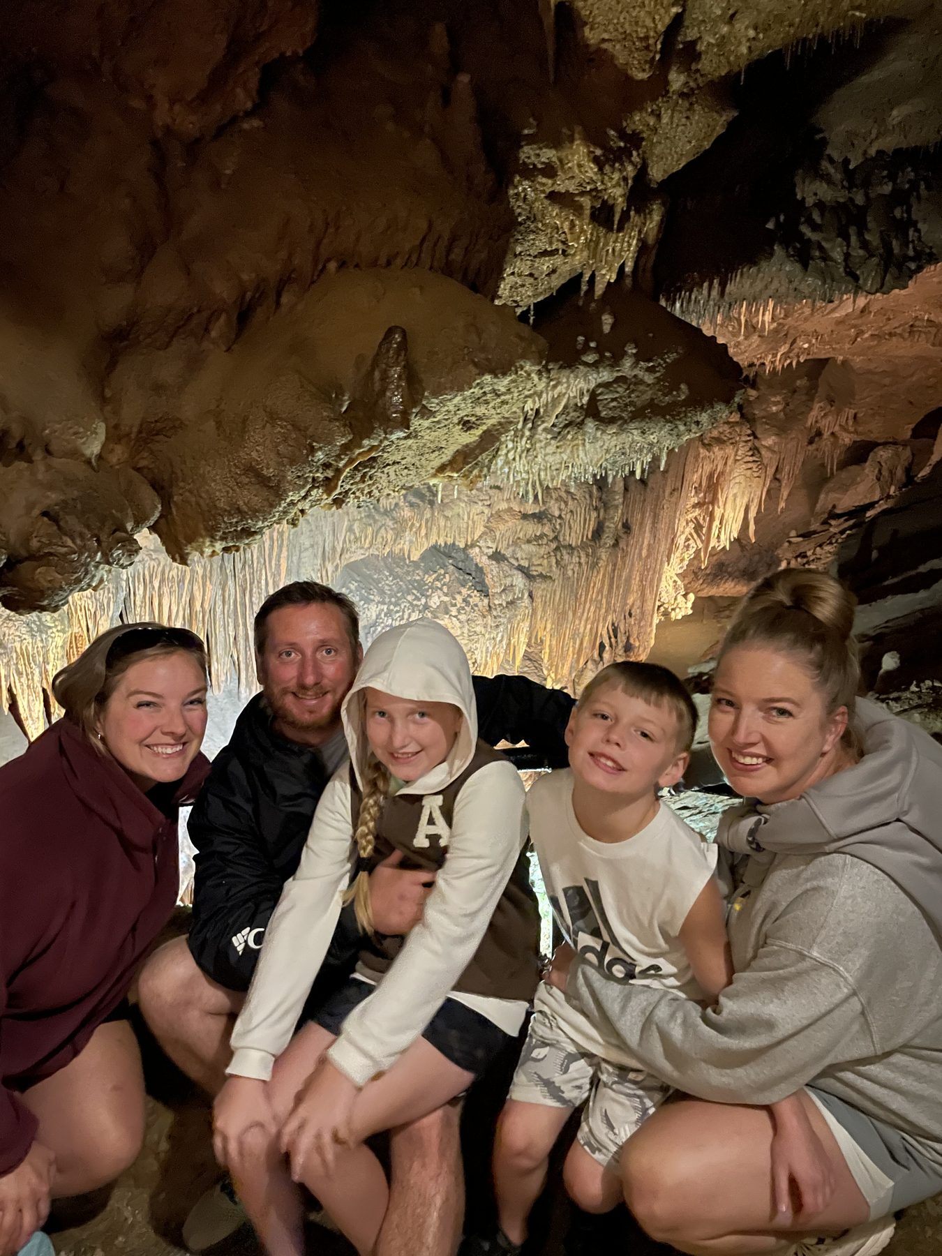 Aleasha crouching with family in a cave, surrounded by lit stalactites and stone formations.