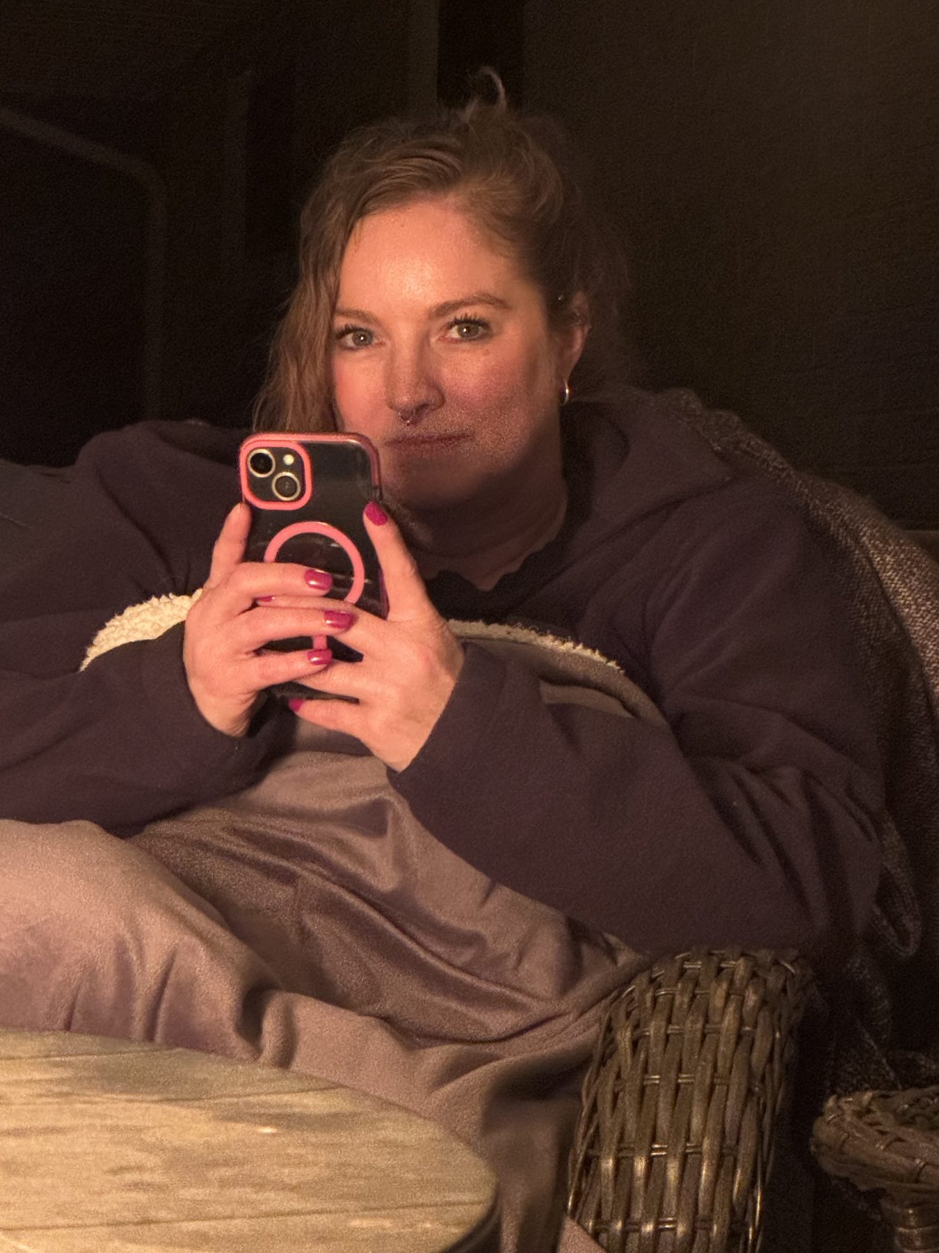 Aleasha wrapped in a blanket on a patio at night, holding a phone in a pink case.
