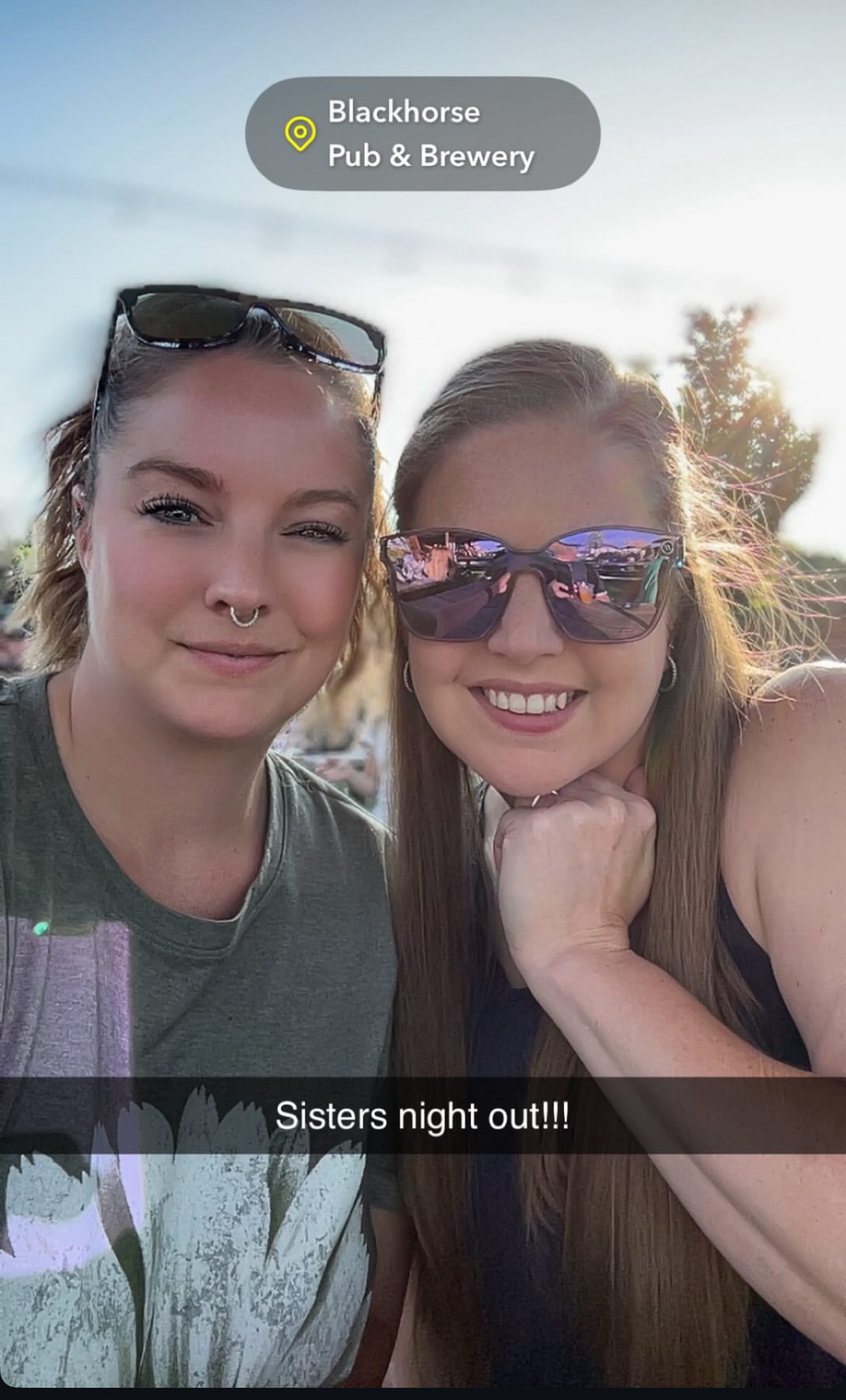 Aleasha and her sister squinting into golden evening sun outside a pub.