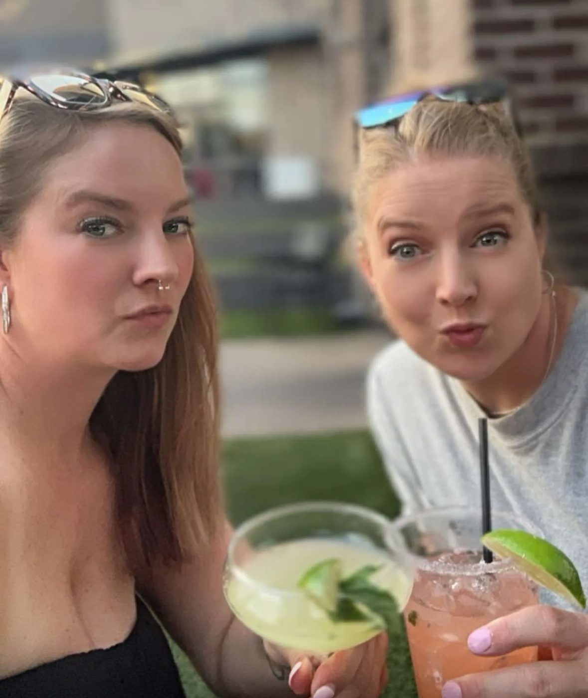 Aleasha and a friend pulling exaggerated serious faces while holding cocktails on a patio.